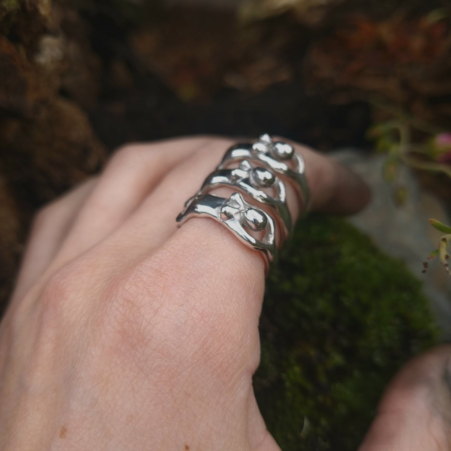 several sterling silver naked body rings being worn against a mossy backdrop