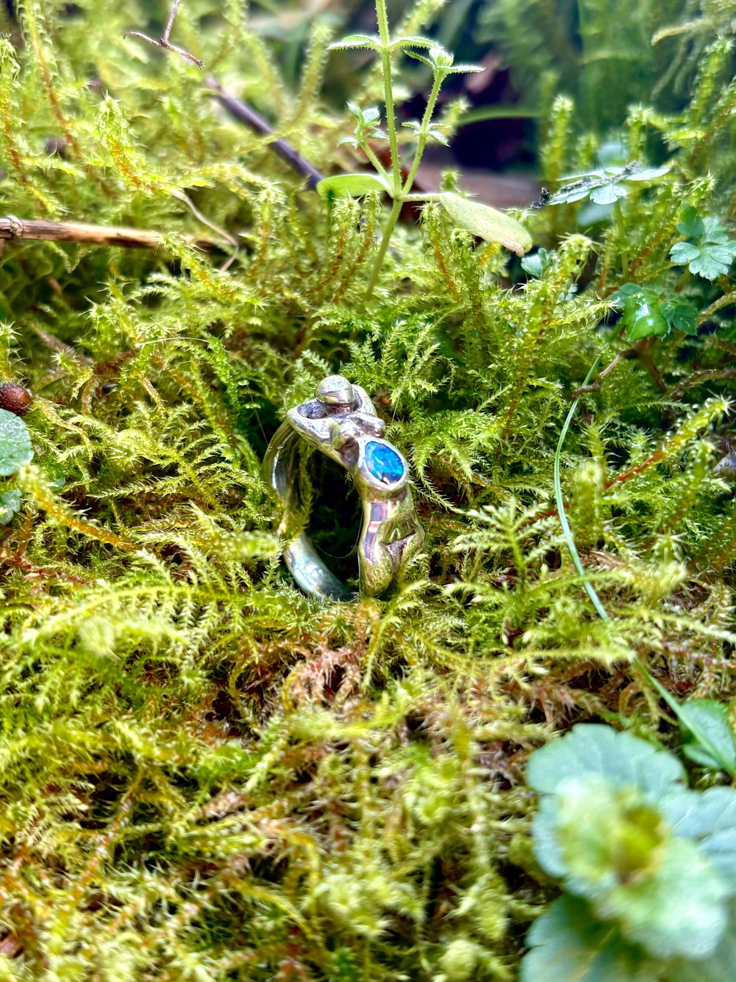 body positive nude female body sterling silver ring with an opal gemstone in her womb on a bed of green moss