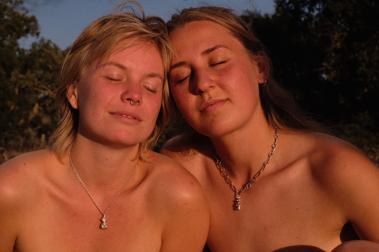 Handmade sterling silver nude female body pendants being worn by two models sat basking in Portuguese sunshine