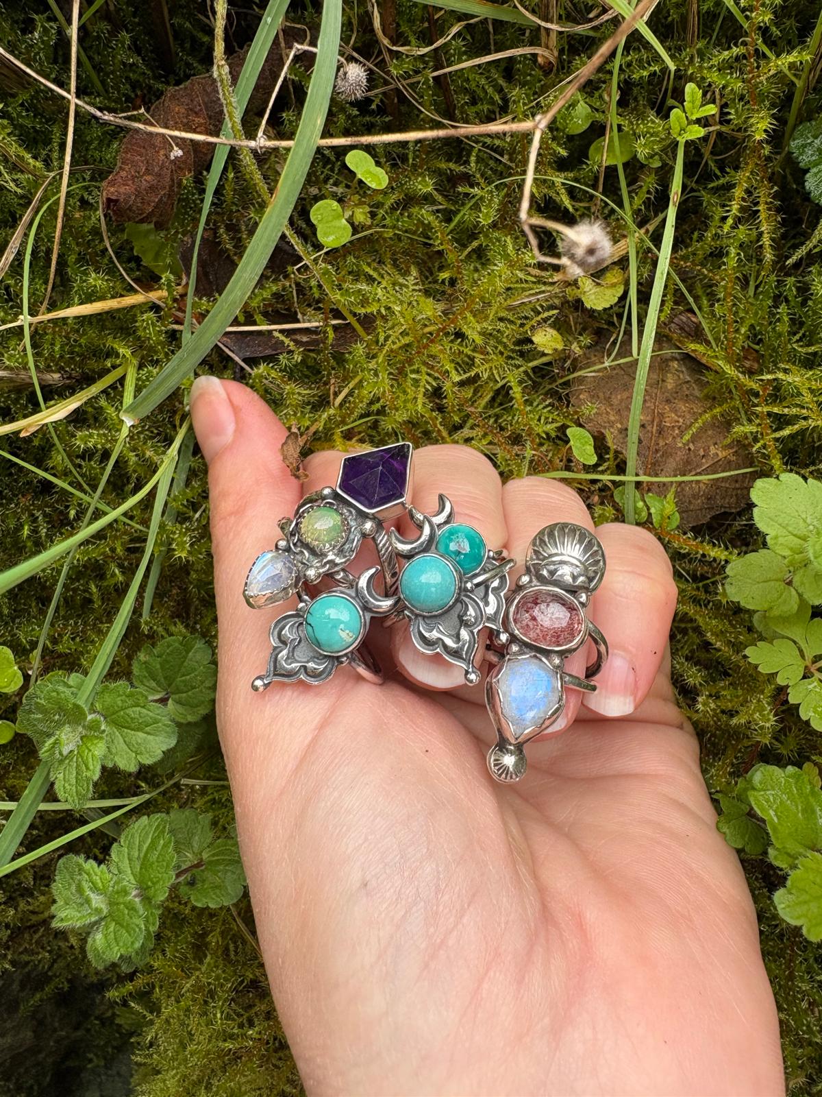 hand holding many sterling silver and gemstone rings