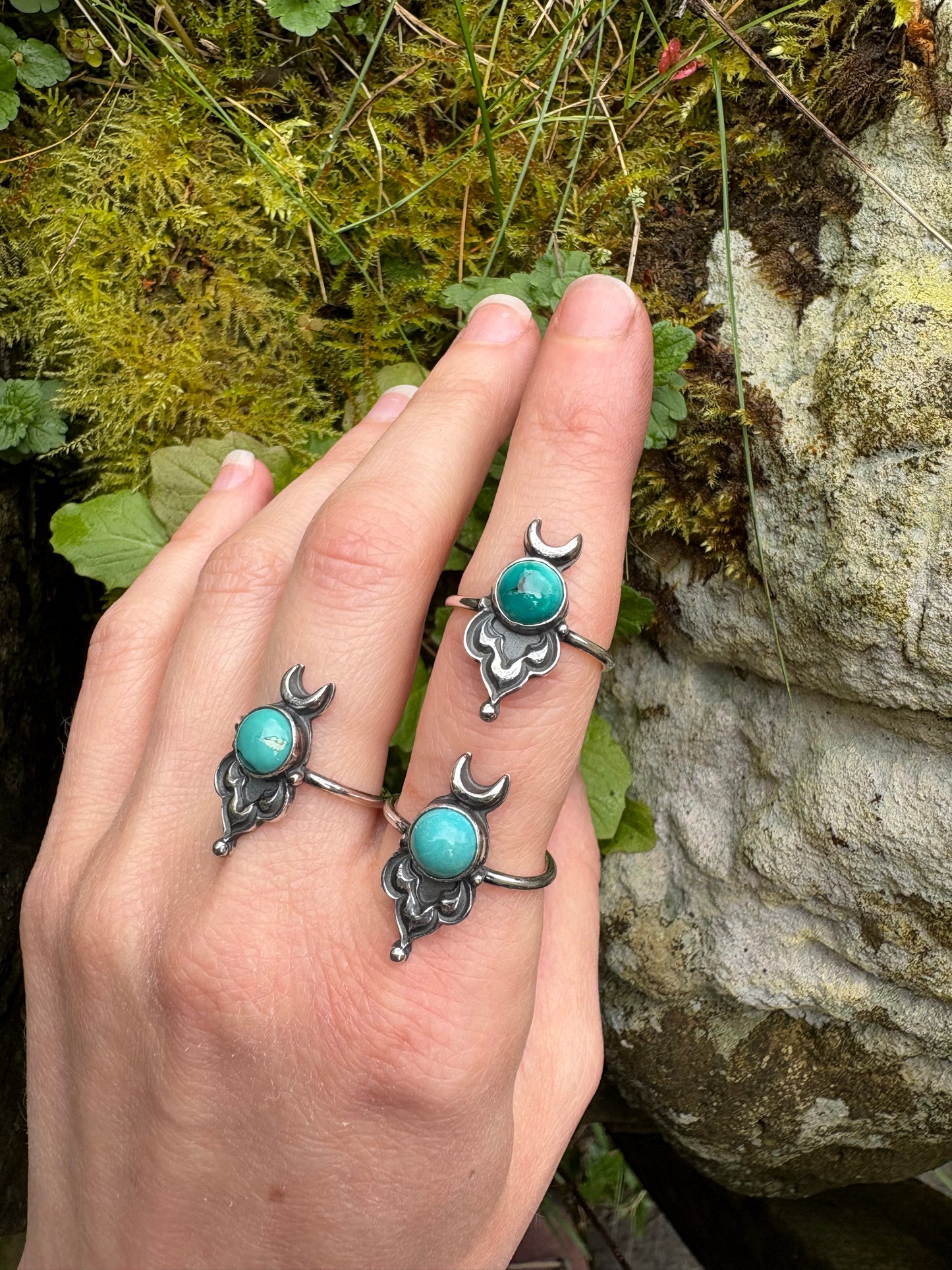 Hand wearing multiple silver rings with turquoise stones against a natural background