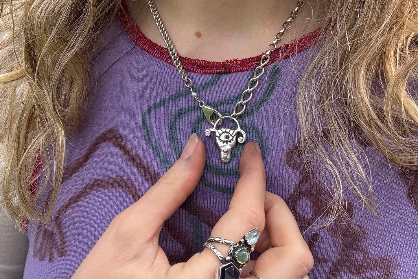 Person wearing a chunky sterling silver uterus pendant necklace, against a purple shirt outdoors
