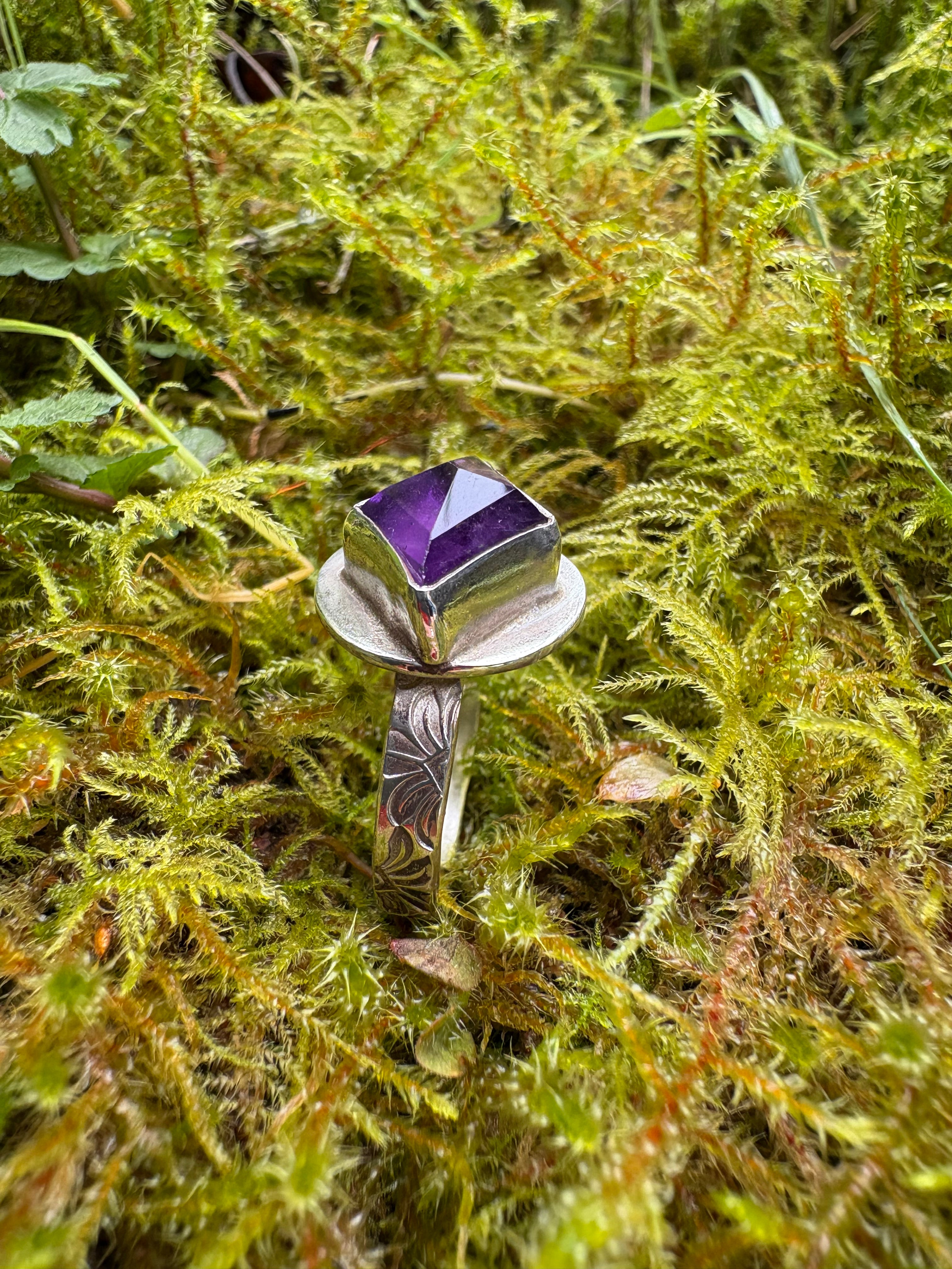 silver ring with bright purple gemstone, nestled in a mossy bed 