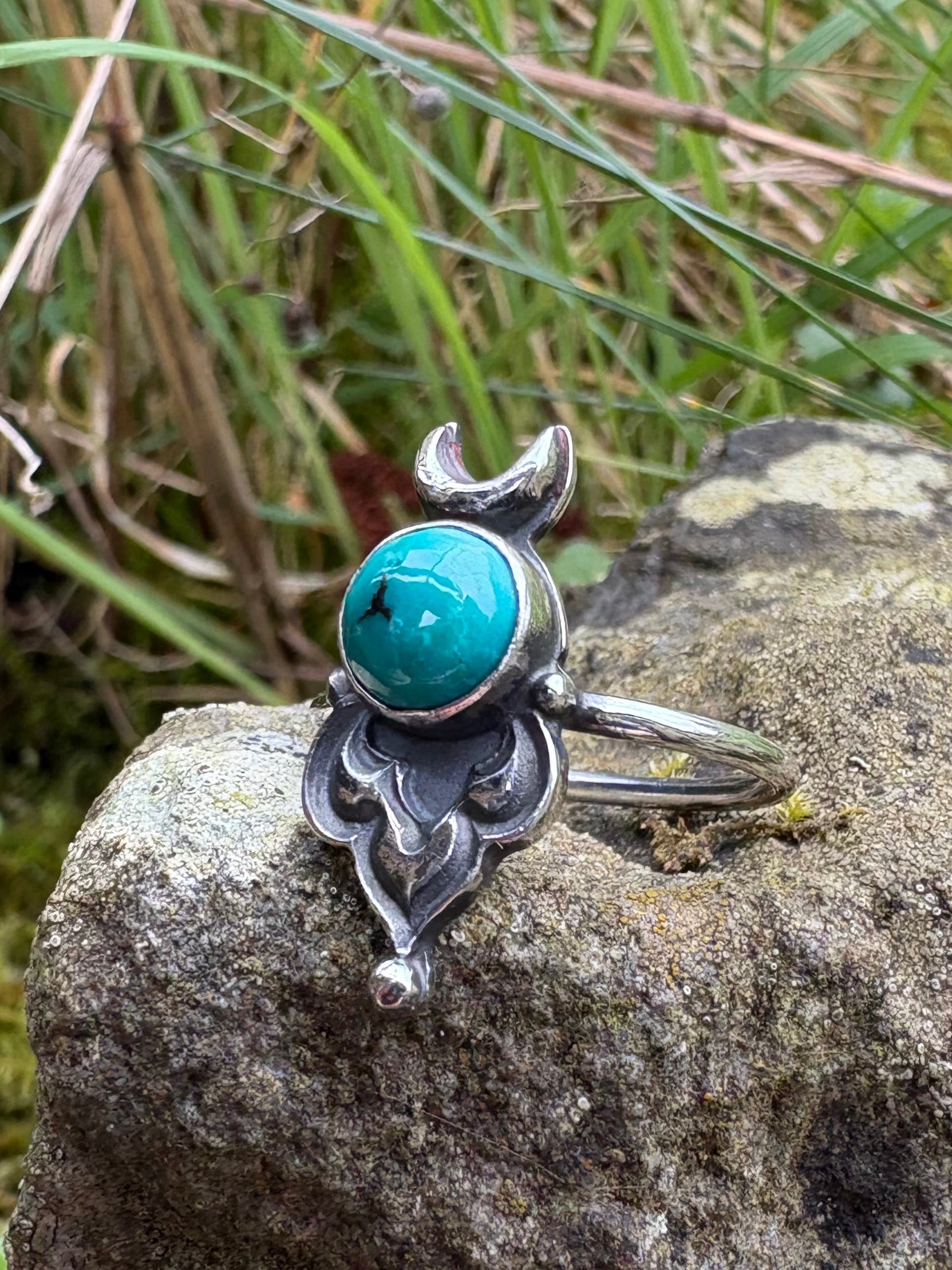 Silver ring with turquoise stone on a rock with grass in the background