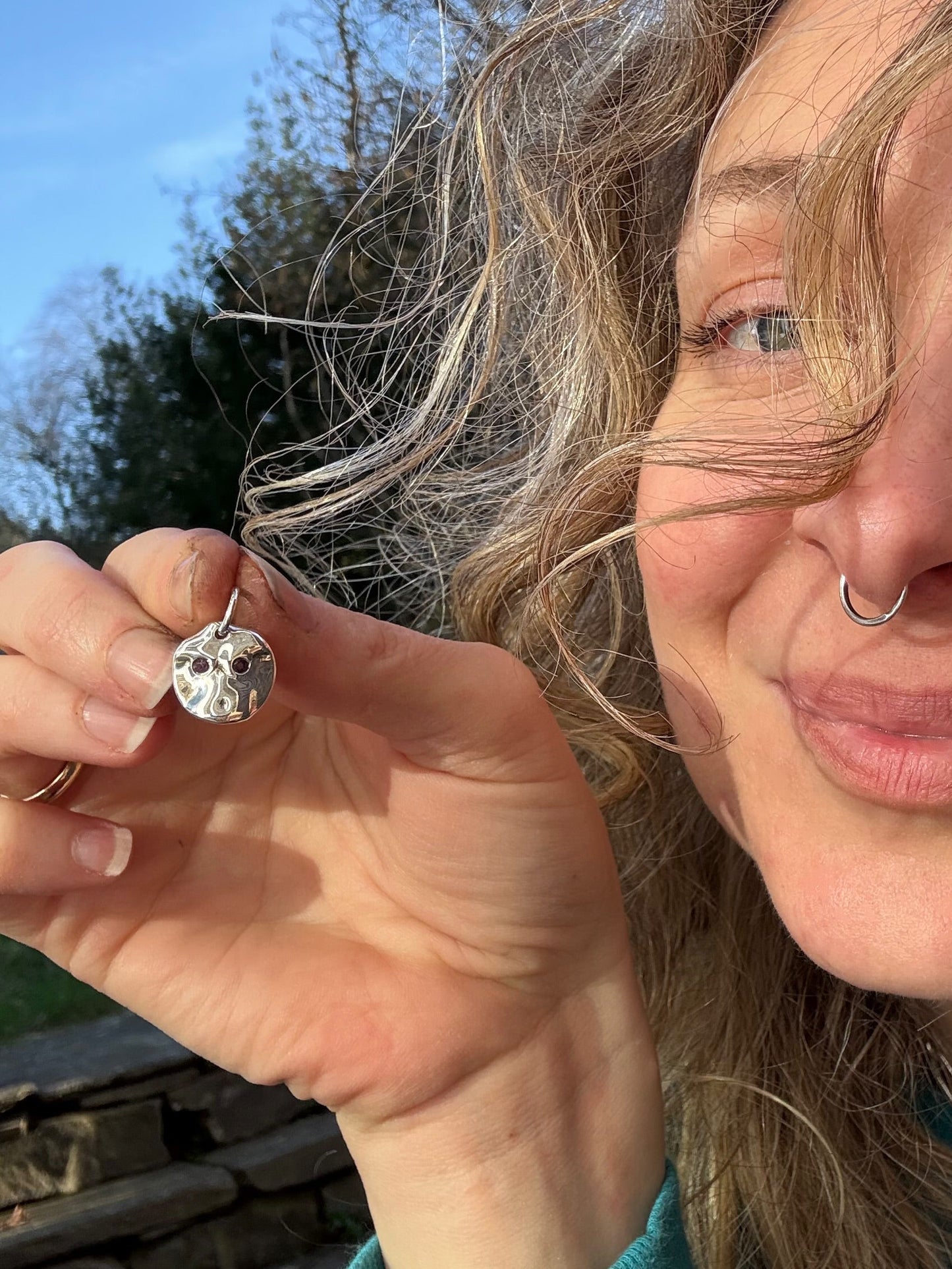 Person holding an amethyst pendant outdoors with trees and blue sky in the background