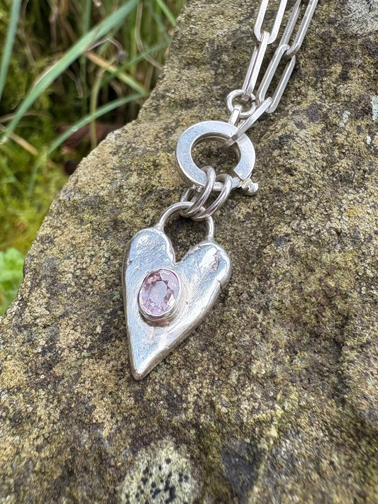 handmade sterling Silver and pink tourmaline necklace with a heart-shaped pendant on a stone surface
