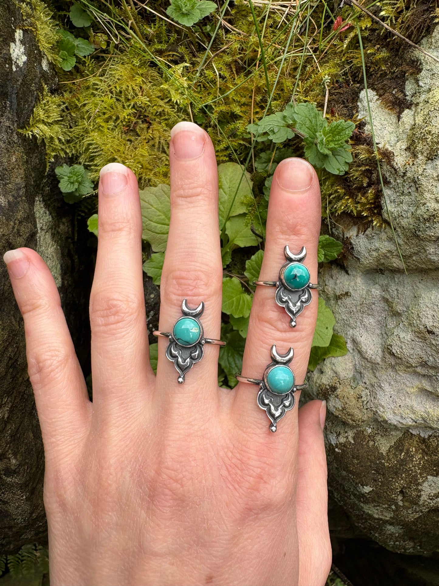 Hand wearing multiple handmade silver rings with turquoise stones against a natural background