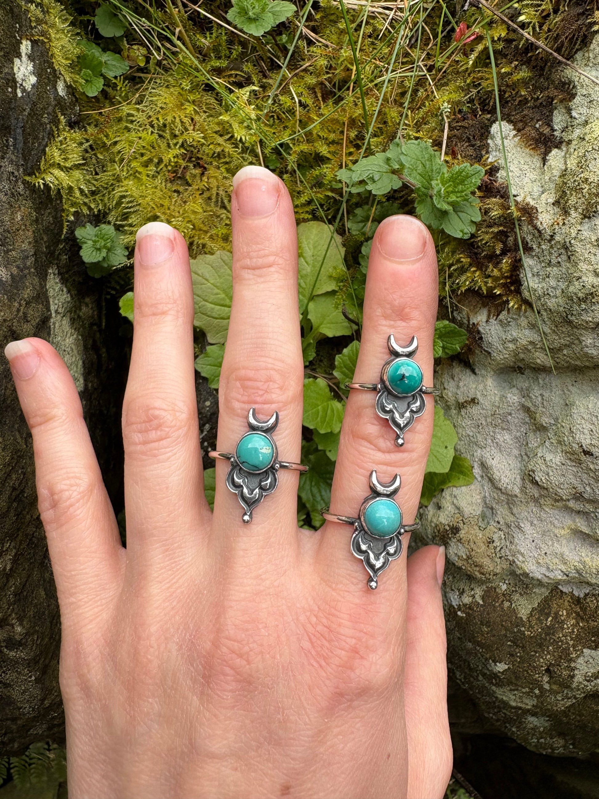 Hand wearing multiple handmade silver rings with turquoise stones against a natural background