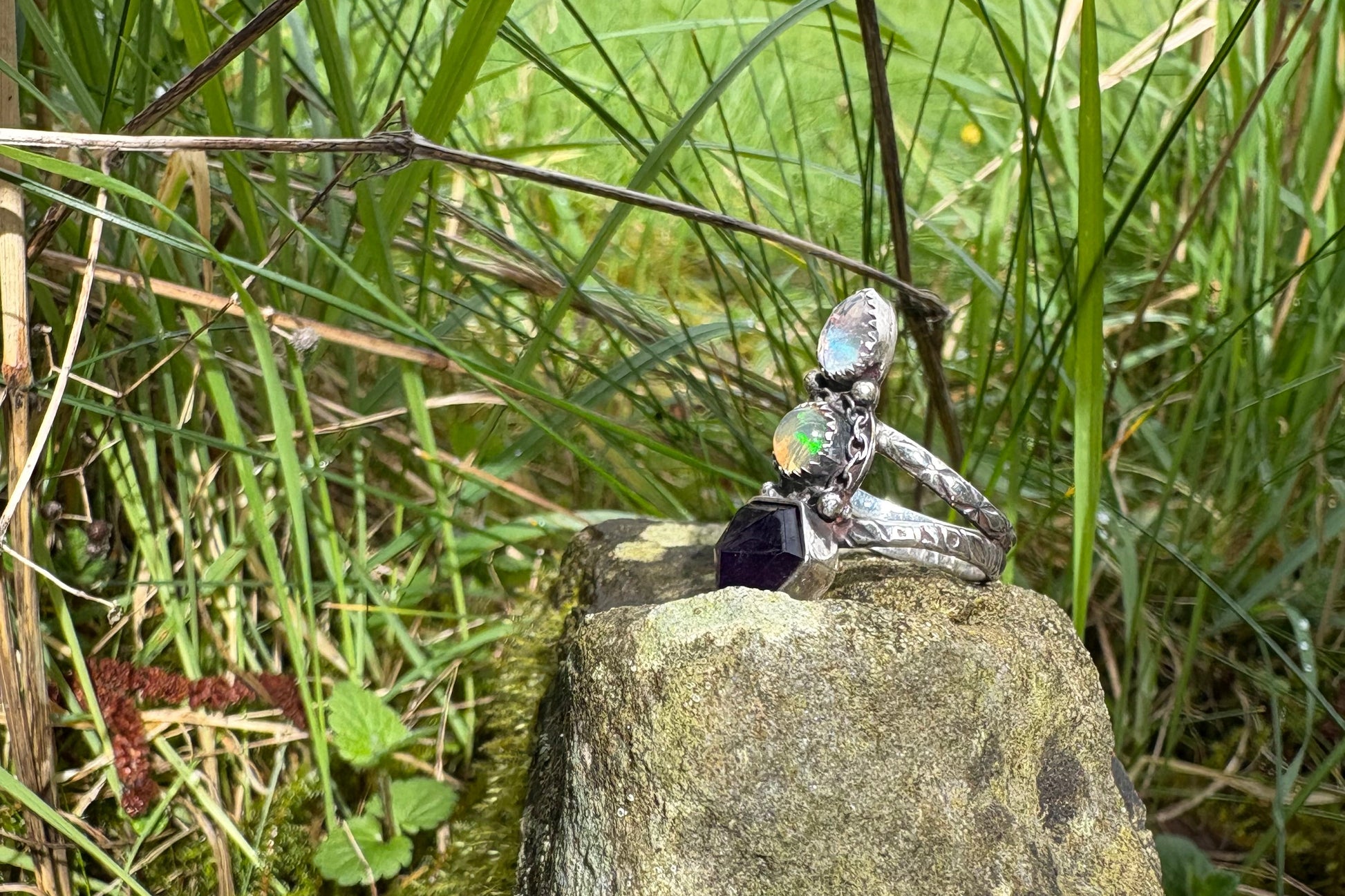 Silver ring with a green stone on a rock surrounded by grass