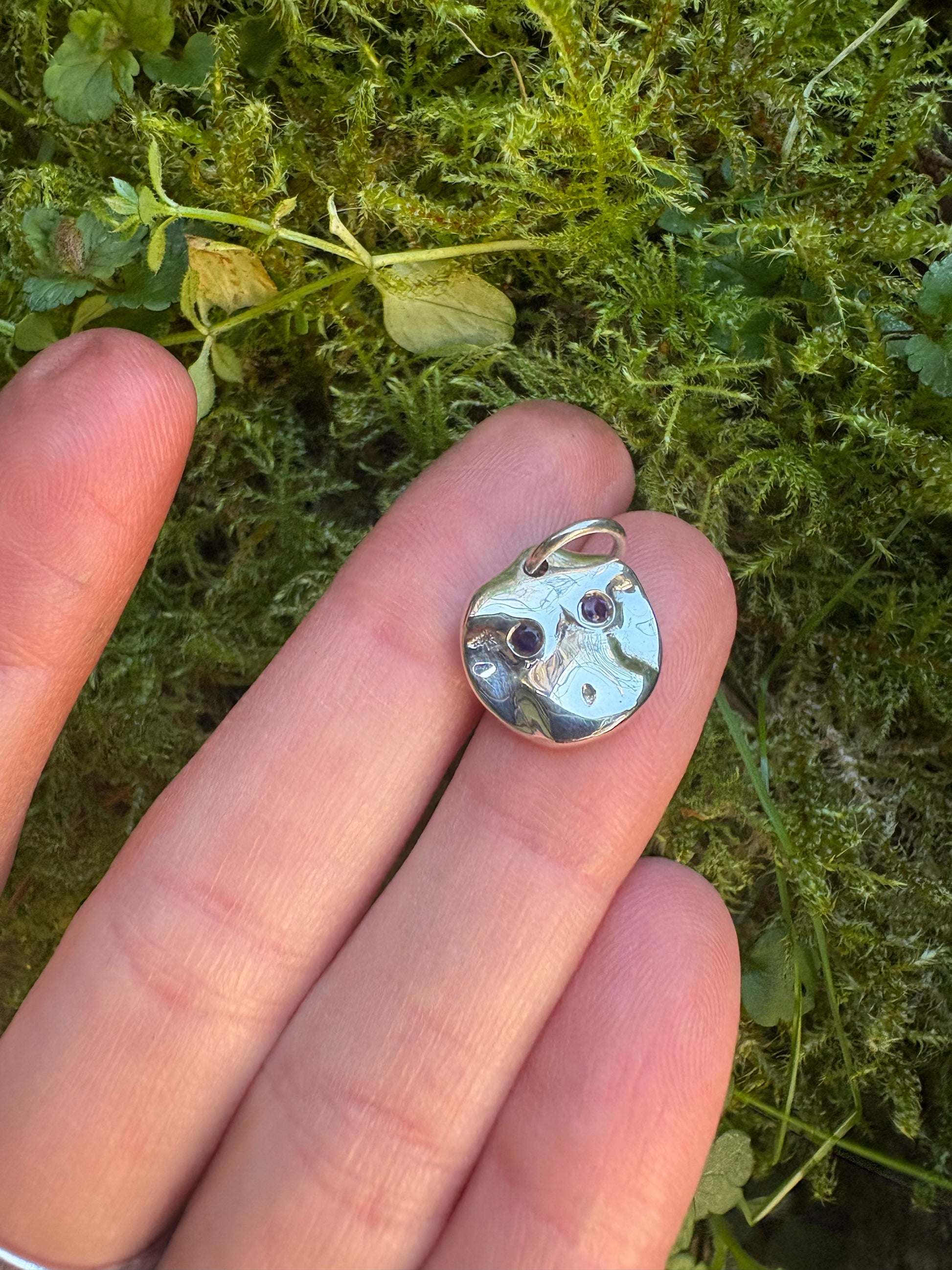 hand holding a pendant of a nude female figure set with two amethysts 