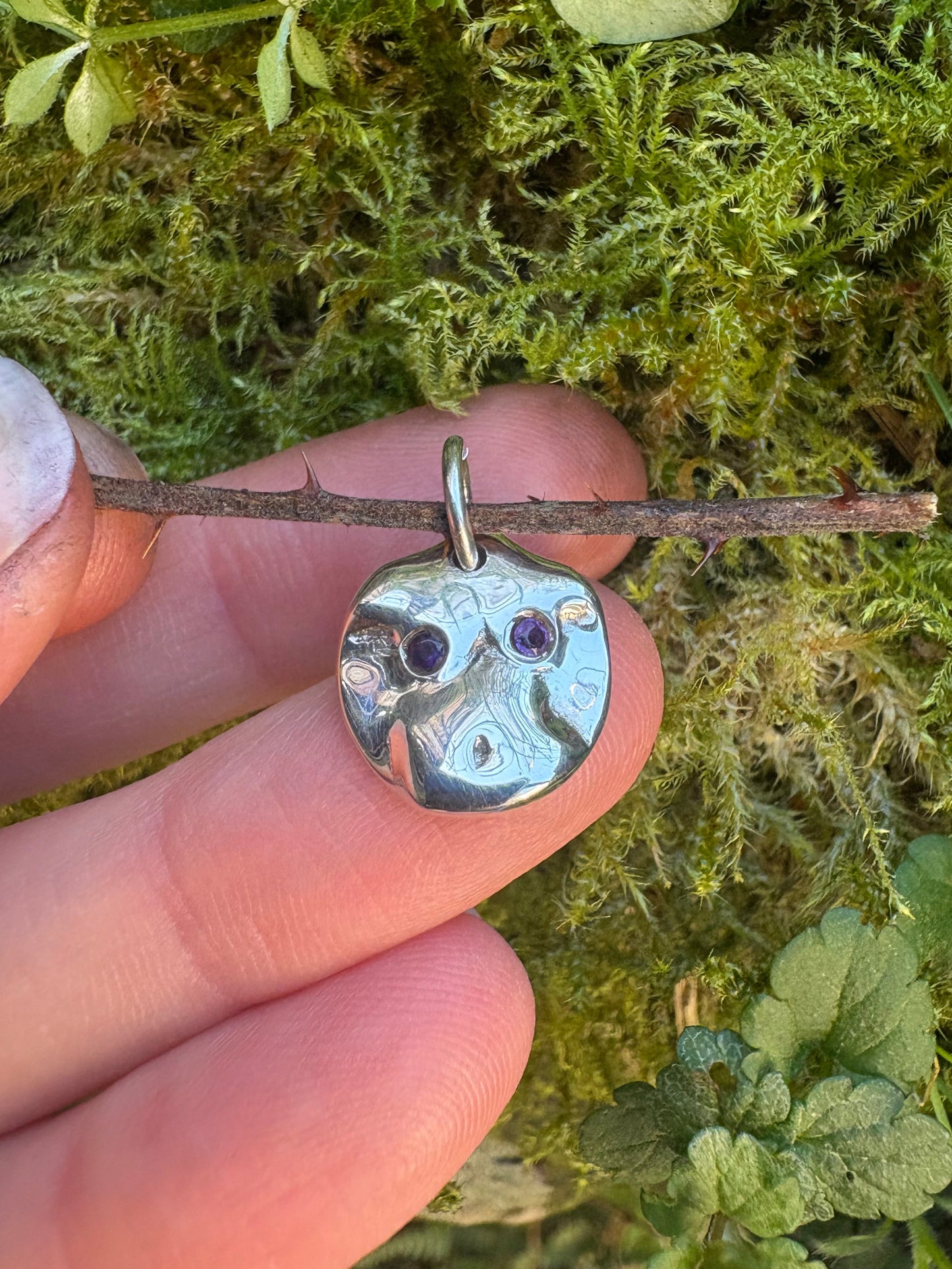 Close-up of a hand holding a silver nude body pendant  with purple amethysts, against a natural background