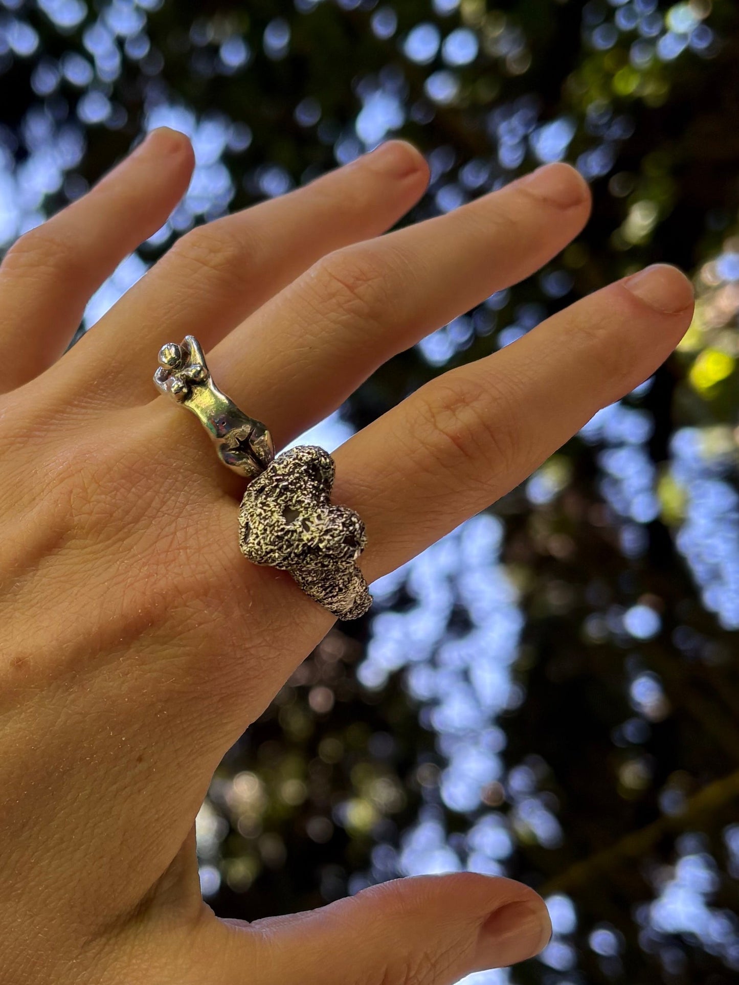 heavy textured heart shaped ring, being worn against tree background. Handmade jewellery, artisan ring, hand carved and cast into silver 