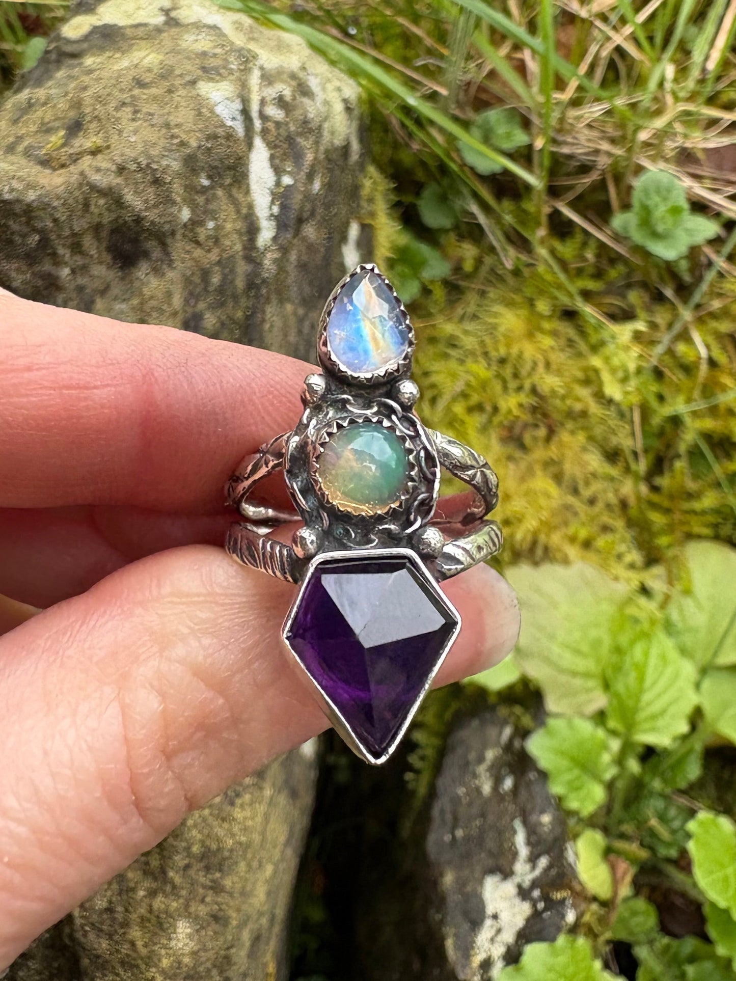Silver ring with gemstones held by a hand against a natural background