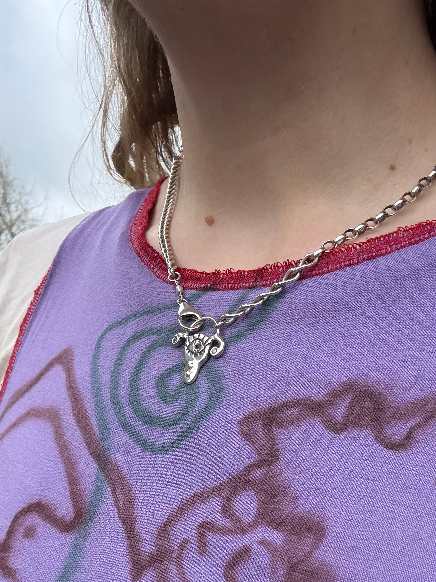 Person wearing a chunky sterling silver uterus pendant necklace, against a purple shirt outdoors