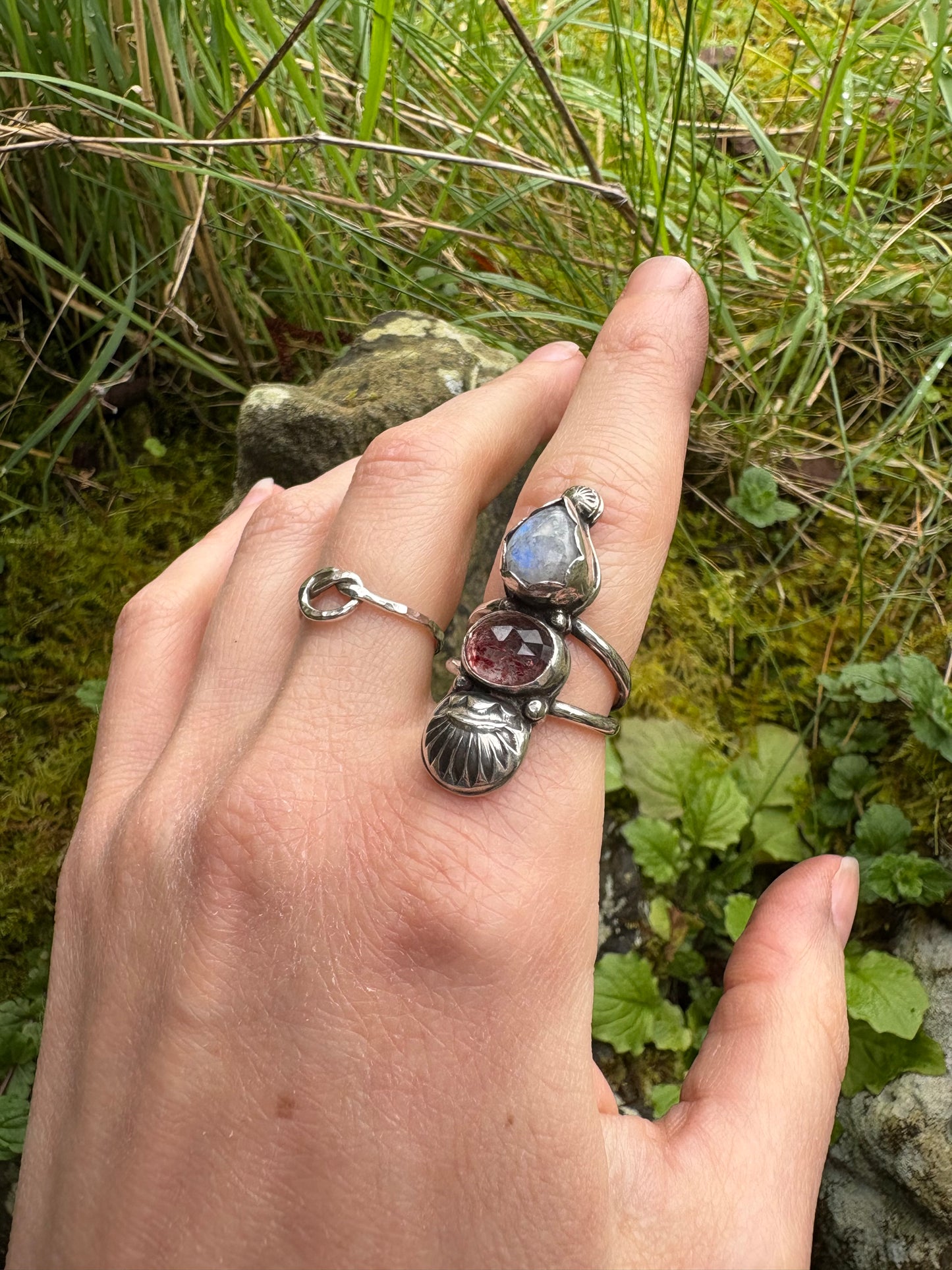 Hand wearing a silver ring with gemstones against a natural background