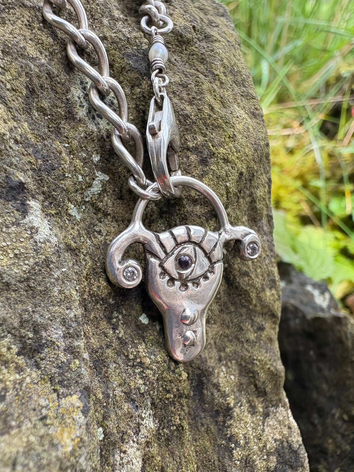 Handmade sterling silver necklace with a detailed uterus pendant with amethyst and cz, 
on a stone surface