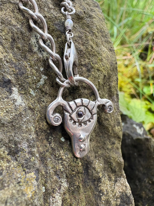 Handmade sterling silver necklace with a detailed uterus pendant with amethyst and cz, 
on a stone surface