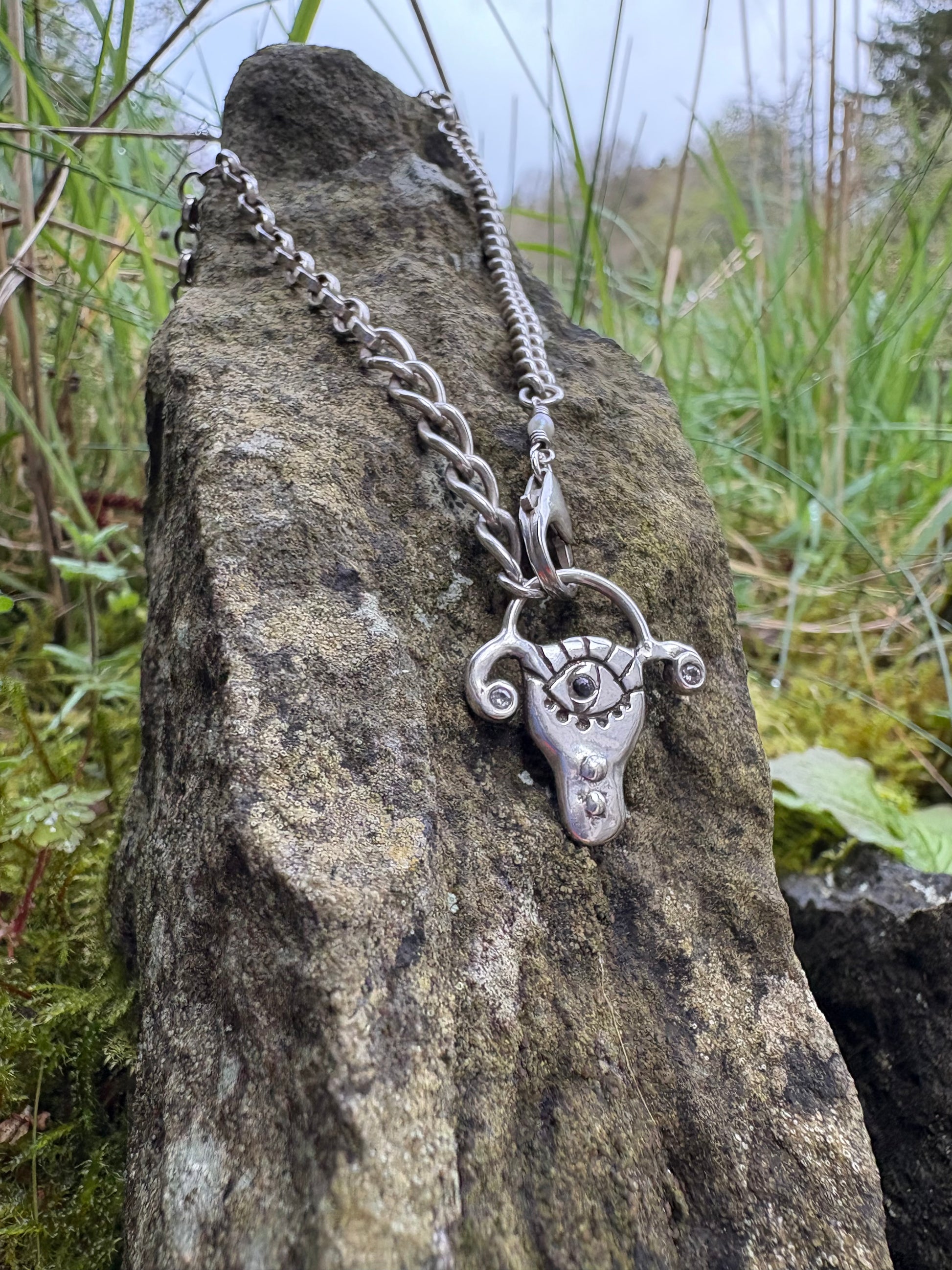Silver pendant uterus pendant, with a carved eye, on a chain lying on a rock with a natural background