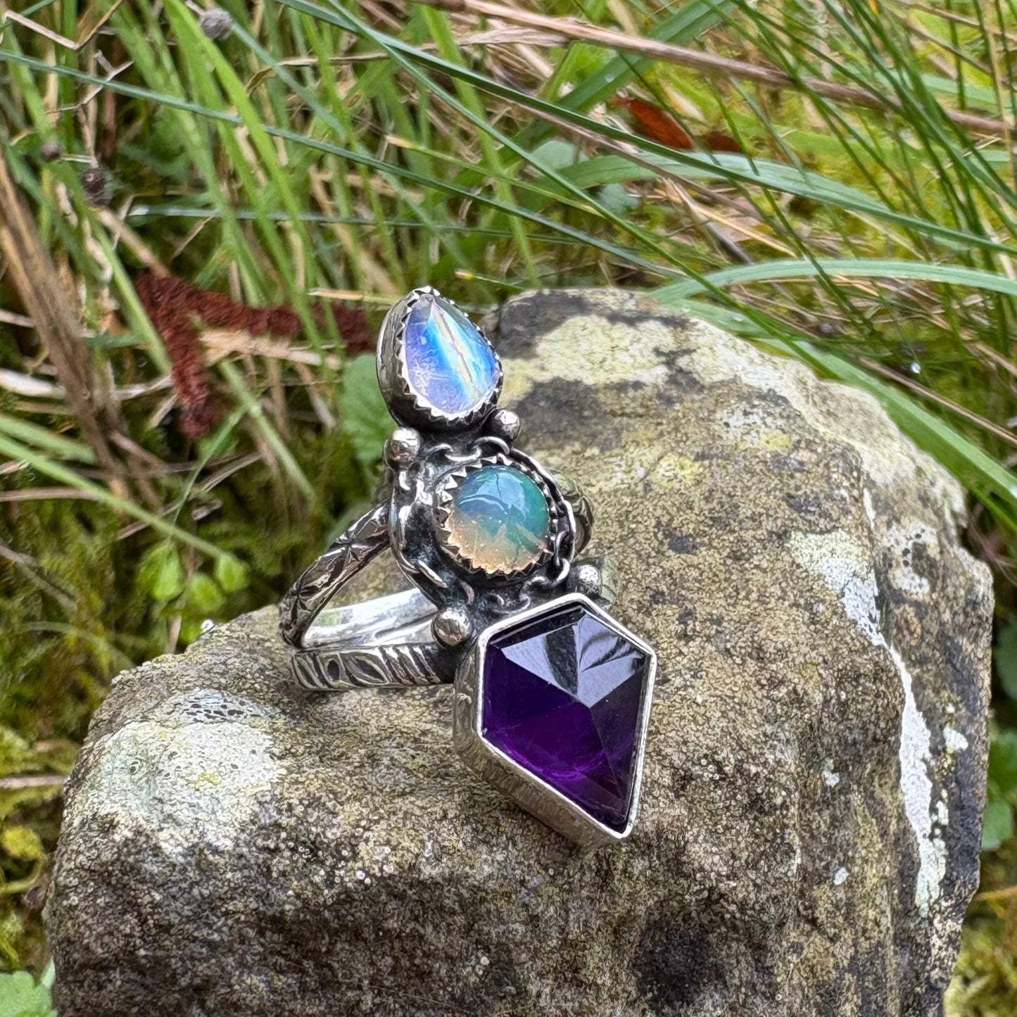 triple gemstone ring, amethyst, opal and moonstone in a sterling silver ring resting on a rock 