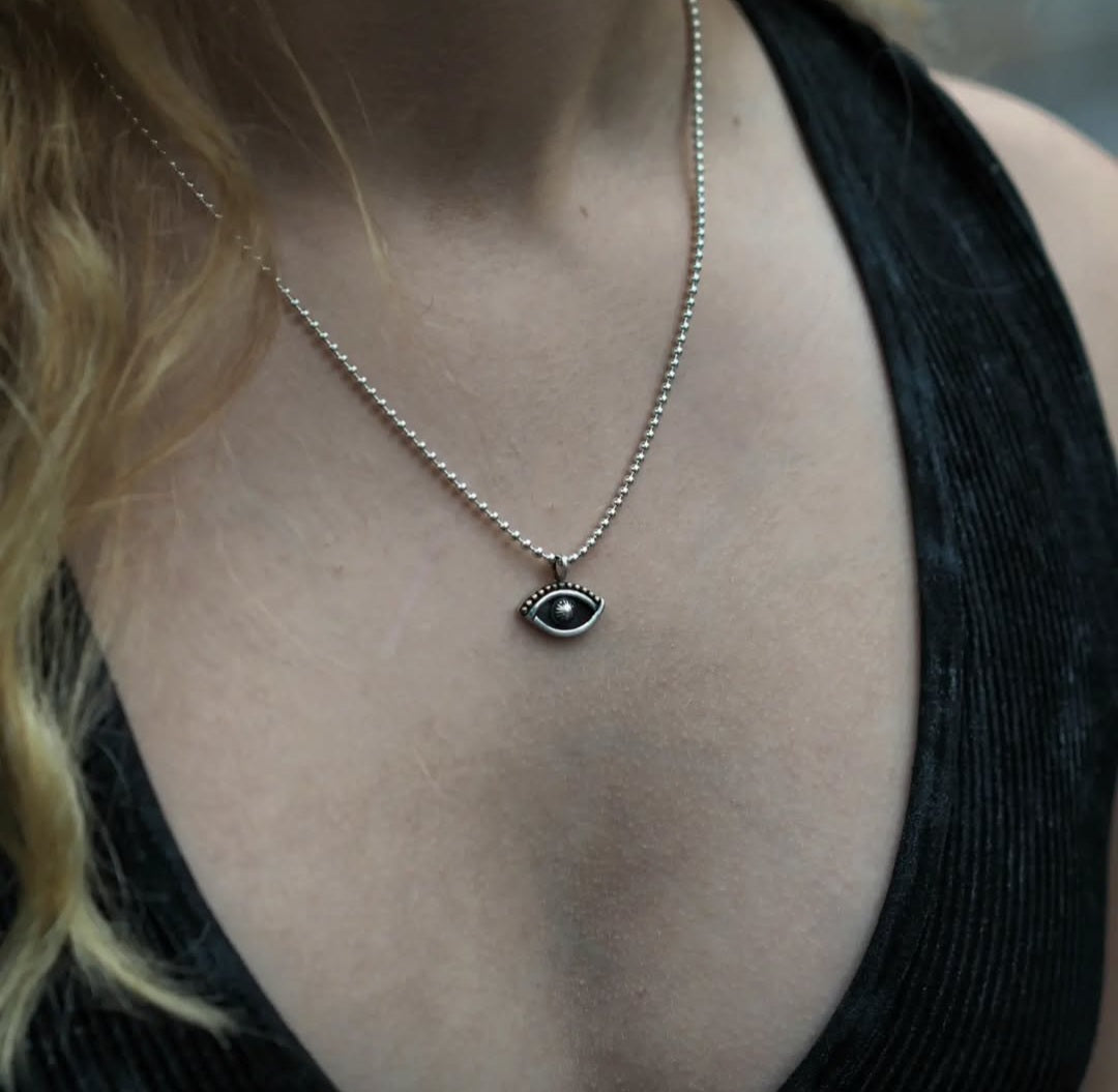 simple and minimalist eye shaped sterling silver pendant on a ball chain worn by a model in a black top 
