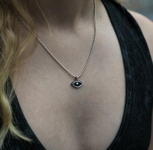 simple and minimalist eye shaped sterling silver pendant on a ball chain worn by a model in a black top 
